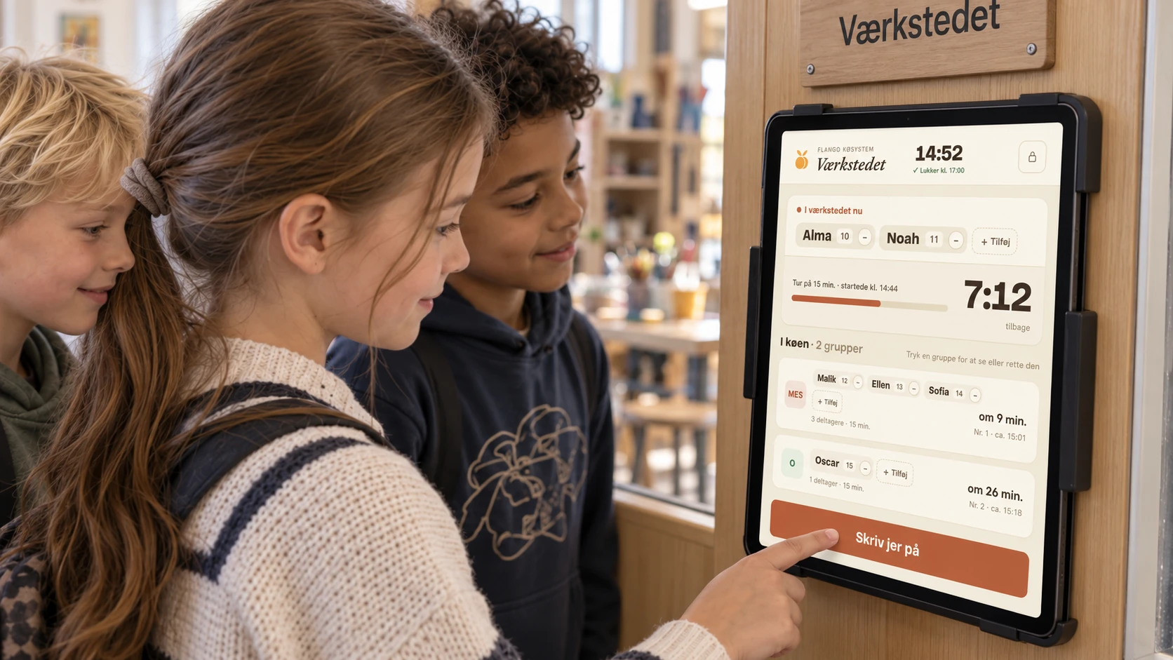 Tre børn skriver sig på Flango Køsystem på en iPad monteret på døren til værkstedet.